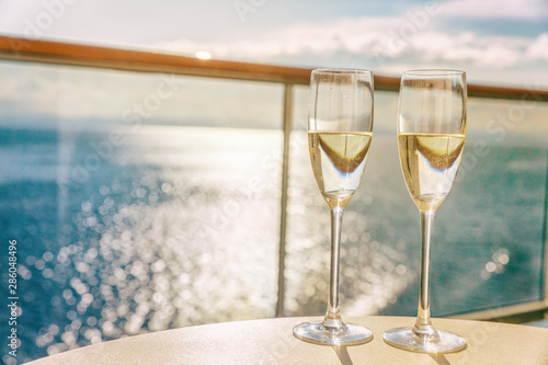 Luxury cruise ship travel champagne glasses on balcony deck with ocean sunset view on Caribbean vacation. Drinks in sun flare on cruise holiday destination.