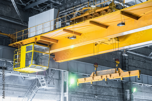 Yellow overhead crane with linear traverse and hooks in engineering plant shop. Cabin of crane operator and jib crab trolley. Landing  staircase. photo