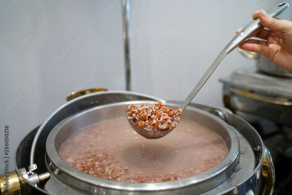 Φωτογραφία Homemade Soft Boiled Red Brown Rice or Rice Porridge - Hand using dipper to ladle congee from hot pot, Traditional Chinese food style and Popular street food in Thailand