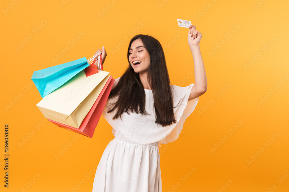 Portrait of glamour shopaholic woman wearing dress smiling while holding credit card and colorful shopping bags Portrait of glamour shopaholic woman wearing dress smiling while holding credit card and colorful shopping bags