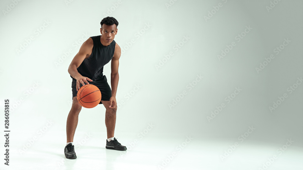 Ready to win. Full length of young african man in sports clothing playing basketball in studio against grey background