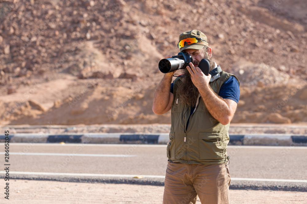 Obraz premium A bearded man on the mountain of Moses with a camera, pilgrimage to the holy places. Nature photographer taking photos in the mountains.