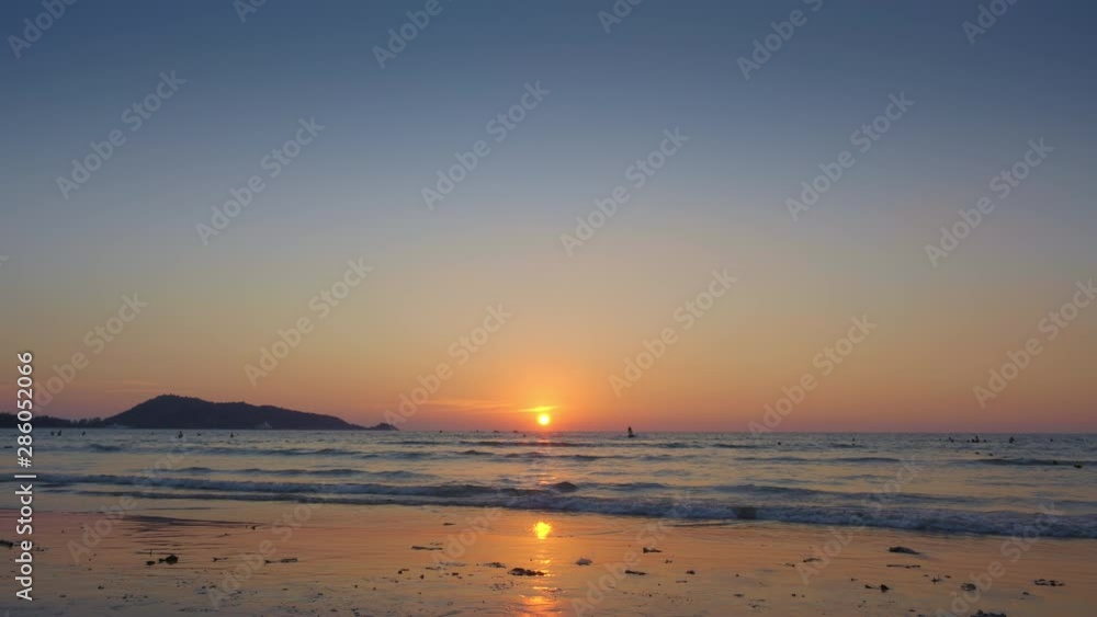 Panorama of a tropical beach with silhouettes of people are swimming in warm water and jet ski during beautiful sunset Panorama of a tropical beach with silhouettes of people are swimming in warm water and jet ski during beautiful sunset