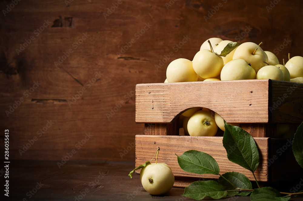 Freshly harvested small apples in box with leaves on wooden background