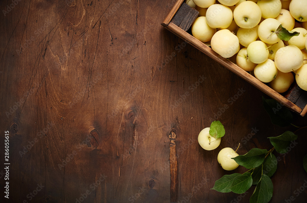 Freshly harvested small apples in box with leaves on wooden background