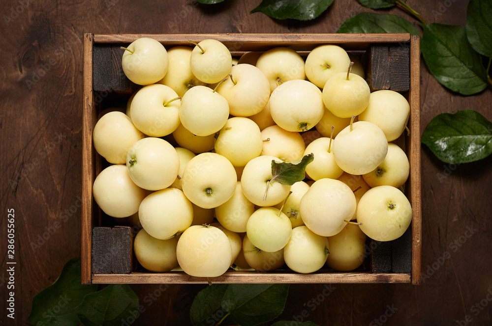 Freshly harvested small apples in box with leaves on wooden background