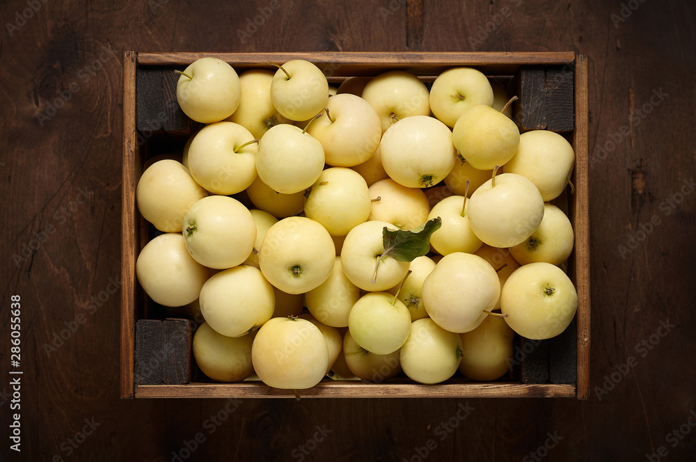 Freshly harvested small apples in box on wooden background