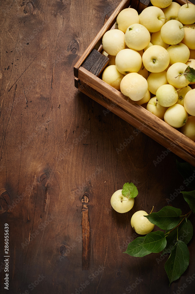 Freshly harvested small apples in box with leaves on wooden background