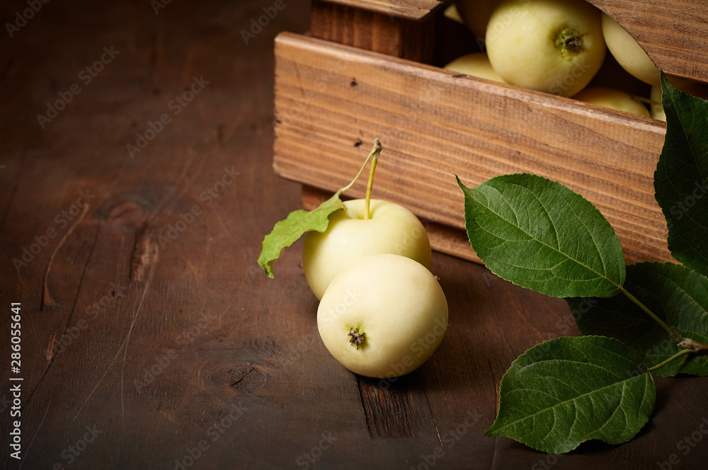 Freshly harvested small apples in box with leaves on wooden background