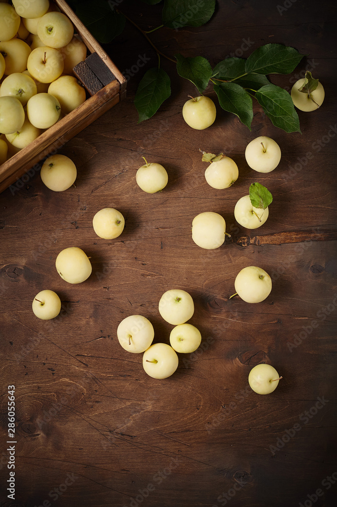 Freshly harvested small apples in box with leaves on wooden background