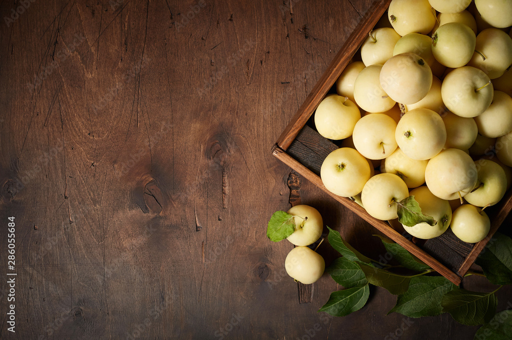 Freshly harvested small apples in box with leaves on wooden background