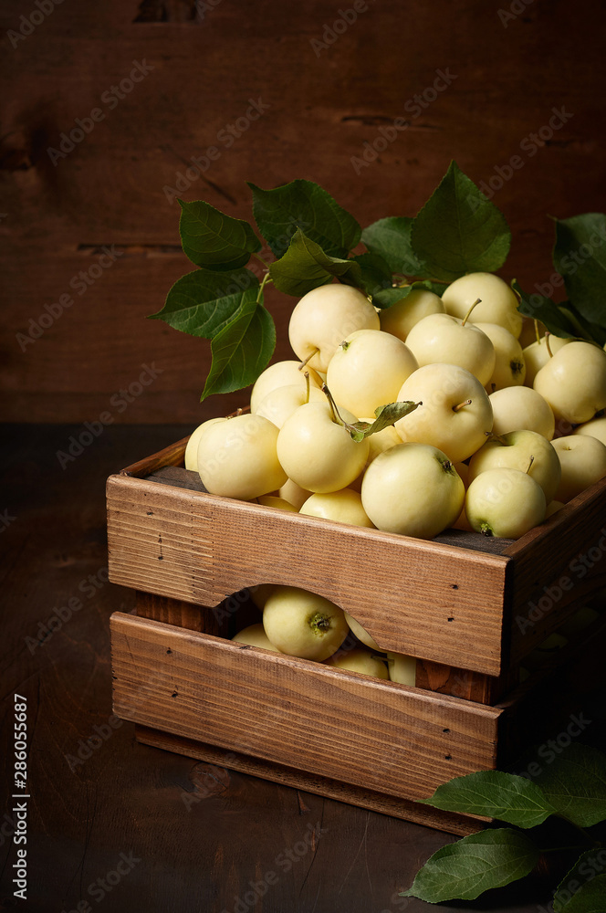 Freshly harvested small apples in box with leaves on wooden background