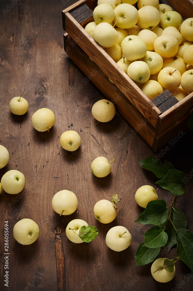 Freshly harvested small apples in box with leaves on wooden background