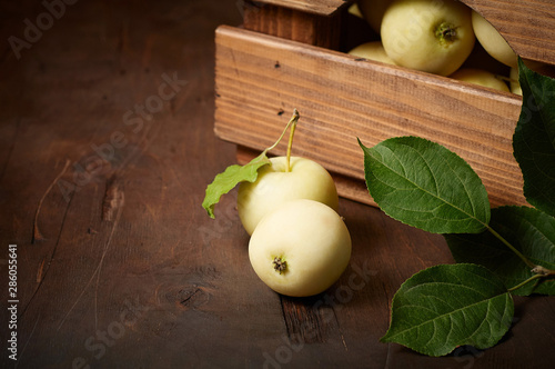 Freshly harvested small apples in box with leaves on wooden background