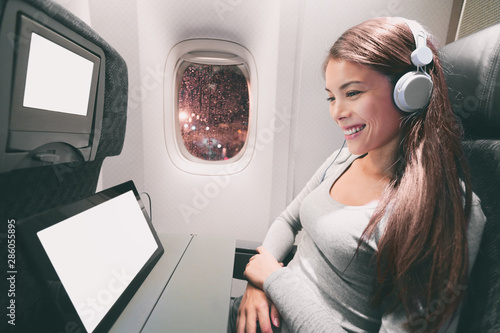 Passenger in airplane using tablet computer. Woman in plane cabin using smart device listening to music on headphones. Banner panorama travel people lifestyle. photo