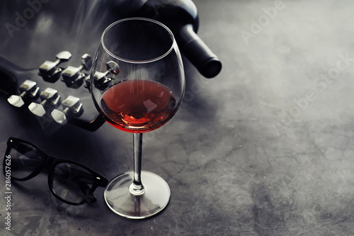 Guitar and high glass with red wine on a stone background.