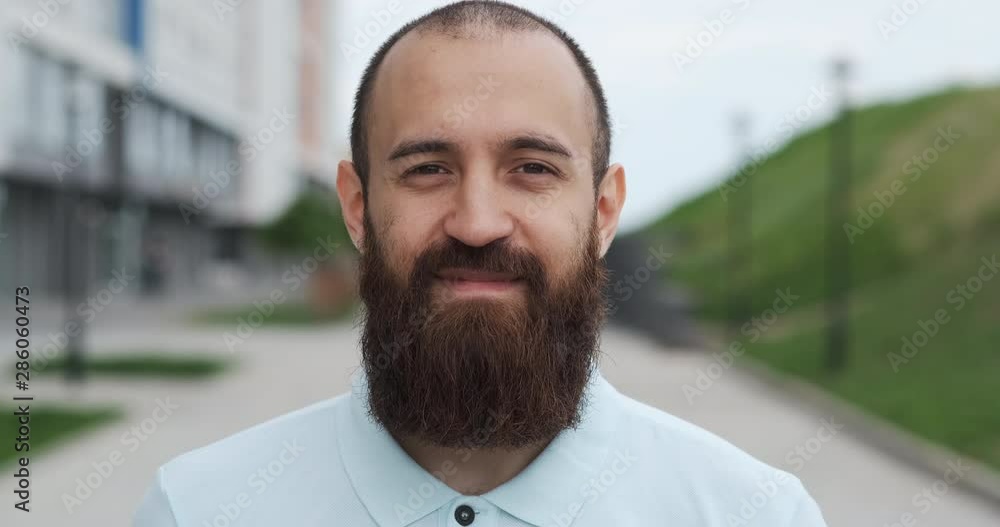 Bearded, balding man stands against backdrop of cityscape and smiles at camera Bearded, balding man stands against backdrop of cityscape and smiles at camera