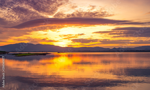 Beautiful golden sky in the morning with sunrise over mountain range and lake or river. Landscape of reservoir and mountain. Peaceful, calm and tranquil background. Stunning and majestic view. © Artinun