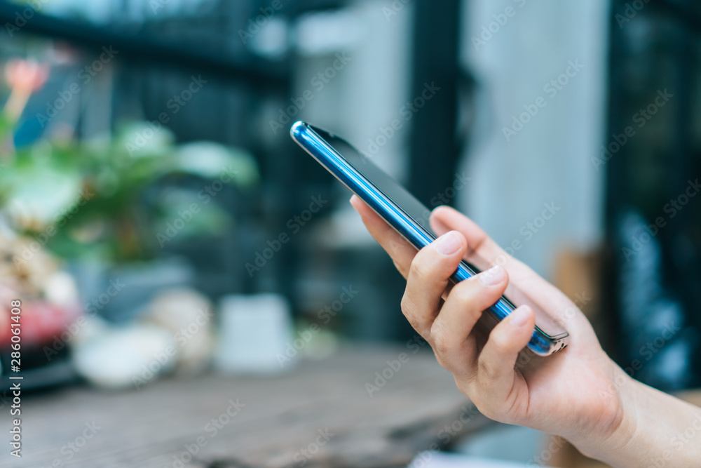 Woman hand using smartphone in cafe shop blur beautiful background. Business stock market and social network concept.