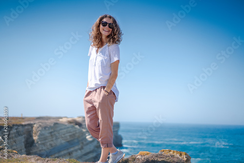 Beautiful young woman with a happy smile in a white T-shirt on the ocean in Portugal