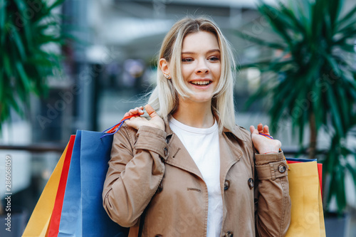 Woman after shopping. Close up portrait of young woman in a brown cloak at a shopping center. Beauty woman with colorful shopping bags in shopping mall. Shopper, sales, shopping center © syrotkin