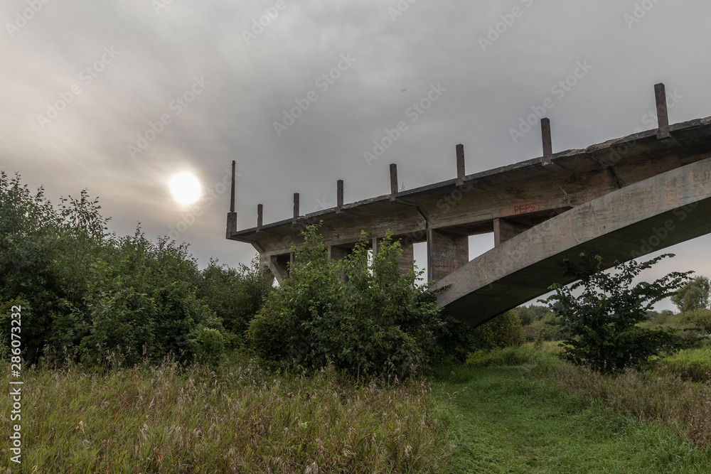 an unfinished bridge stands on the river in the meadow
