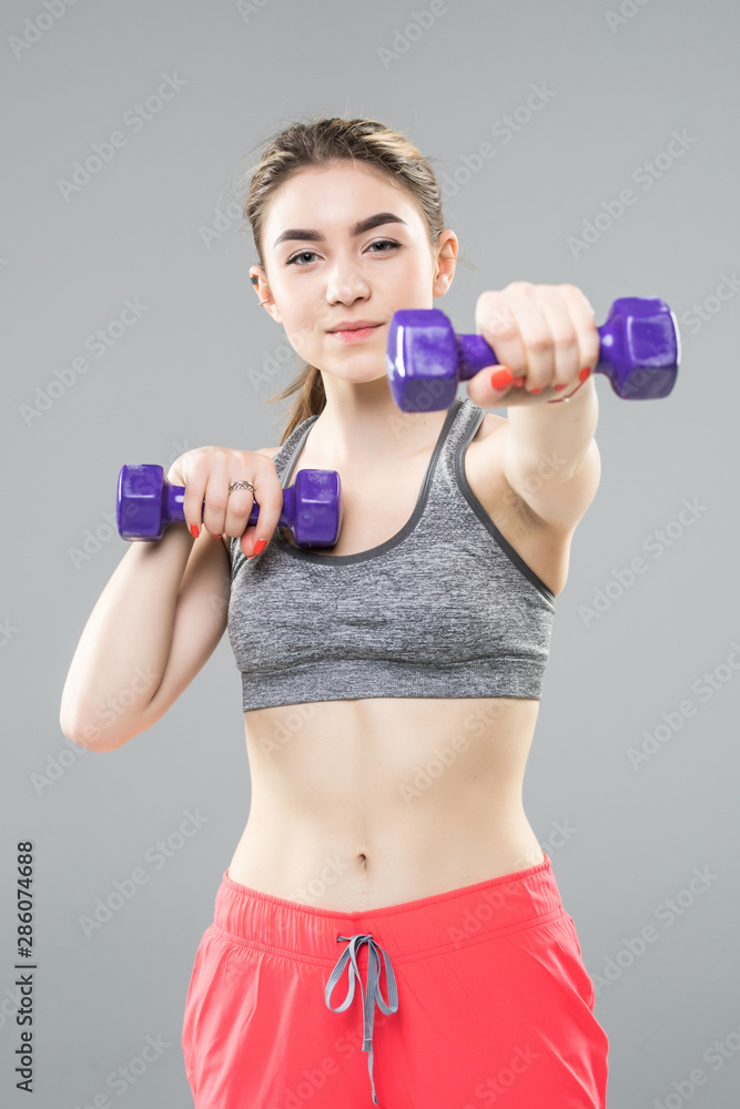 Athletic woman doing exercise for arms muscular fitness model working out with dumbbells on grey background. Strength and motivation Athletic woman doing exercise for arms muscular fitness model working out with dumbbells on grey background. Strength and motivation