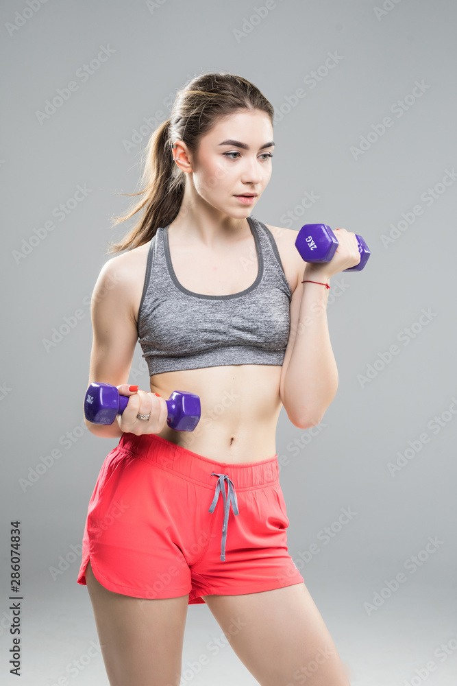 Athletic woman doing exercise for arms muscular fitness model working out with dumbbells on grey background. Strength and motivation Athletic woman doing exercise for arms muscular fitness model working out with dumbbells on grey background. Strength and motivation
