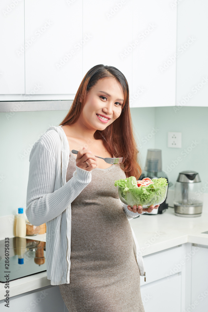 Portrait of beautiful young pregnant woman eating fresh healthy salad for lunch