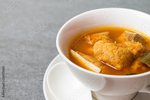 Spicy soup or orange curry of Thai with fish in white bowl and spoon on concrete table.