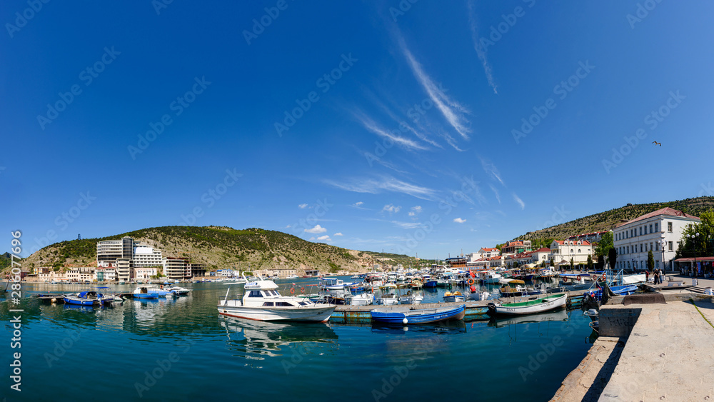 The promenade of the city of Balaklava on a bright sunny day with many parked yachts and boats.