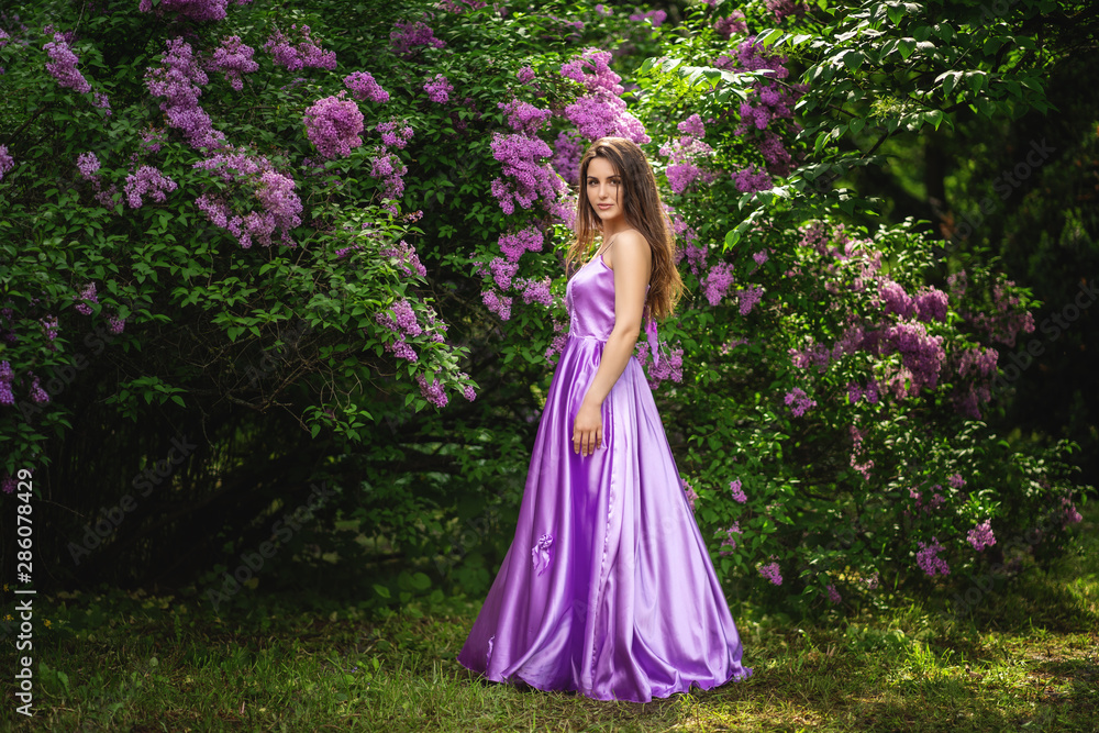 Beautiful young woman in long dress near blossom trees in spring garden