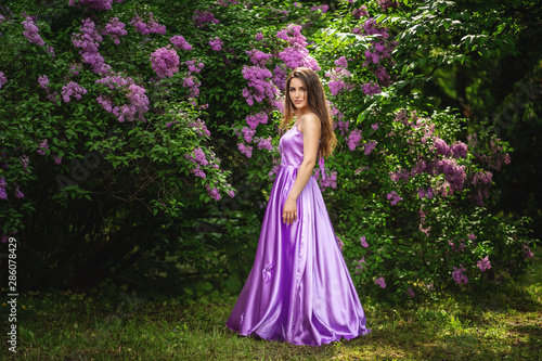 Beautiful young woman in long dress near blossom trees in spring garden