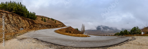 Mountain road in the fall on a foggy cloudy autumn day with clouds in the sky.