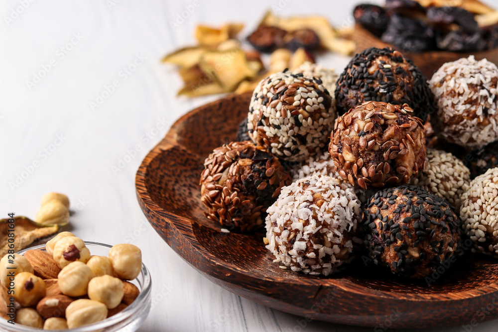 Healthy energy balls of nuts, oatmeals and dried fruit with coconut, flax and sesame seeds on coconut wooden plate on a white background, horizontal orientation, closeup Healthy energy balls of nuts, oatmeals and dried fruit with coconut, flax and sesame seeds on coconut wooden plate on a white background, horizontal orientation, closeup