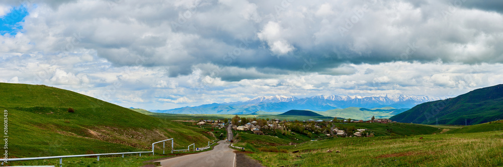 road stretching into the distance against the backdrop of a mountain with snow-capped peaks on a sunny day with clouds in the sky.