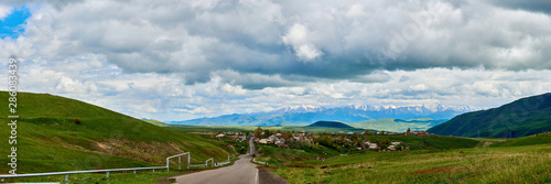 Fototapeta Naklejka Na Ścianę i Meble -  road stretching into the distance against the backdrop of a mountain with snow-capped peaks on a sunny day with clouds in the sky.