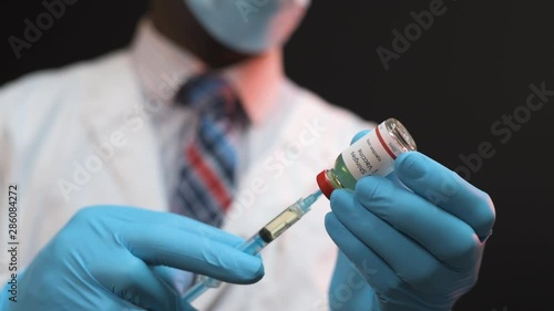 African American doctor drawing vaccine from vial into a syringe on a black background wearing white coat and blue gloves with mask photo