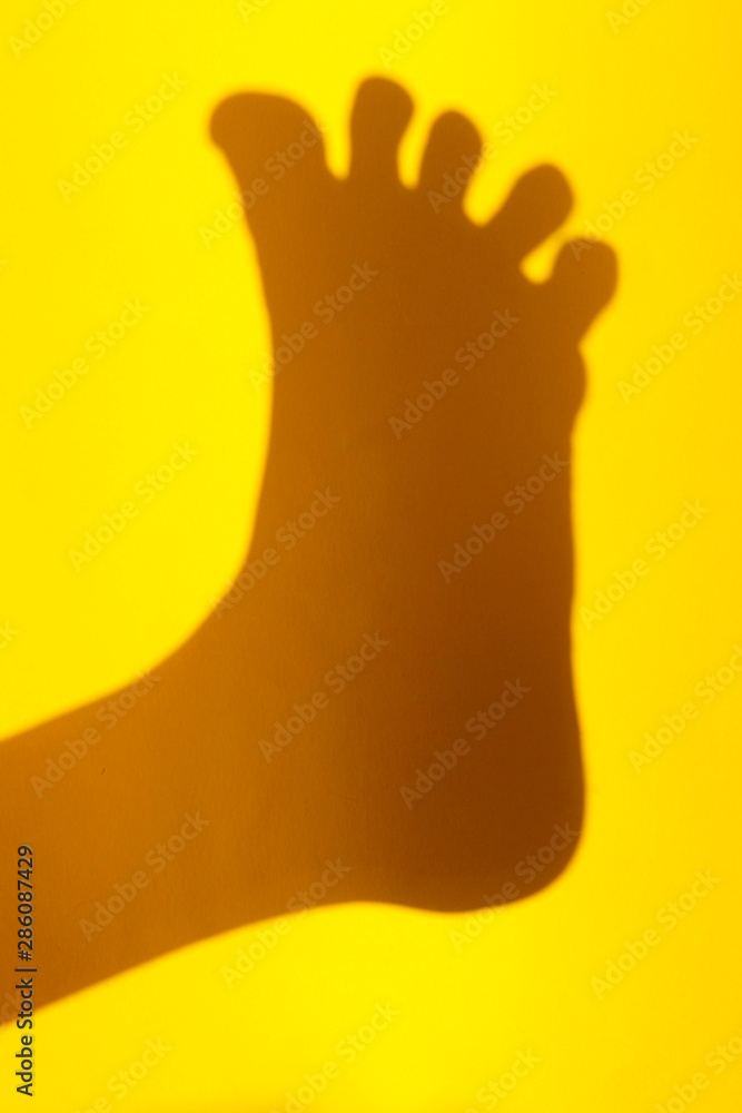 Blurred image of a foot shadow on the yellow wall. Abstract background. Body part. Blurred image of a foot shadow on the yellow wall. Abstract background. Body part.