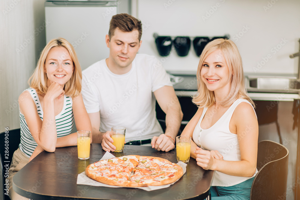 Young friends eating pizza in kitchen and smiling Young friends eating pizza in kitchen and smiling