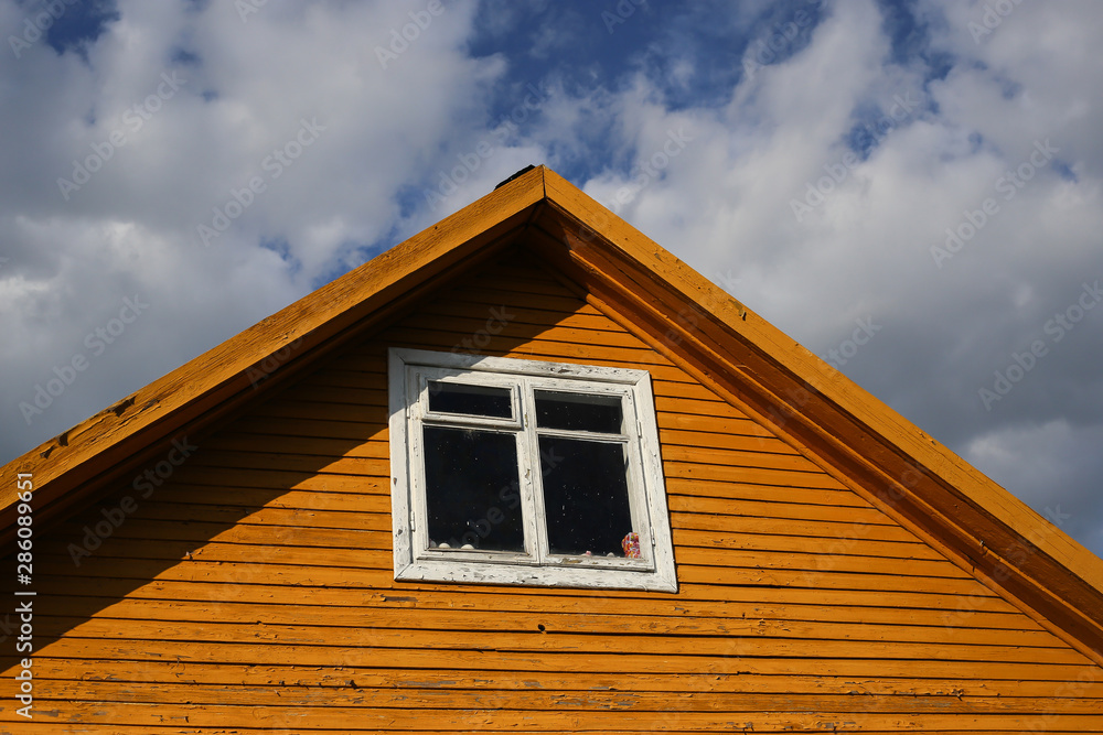 Triangular roof with yellow wooden walls and white windows and blue sky background. Part of typical house in Lithuania, Trakai. Antique old house