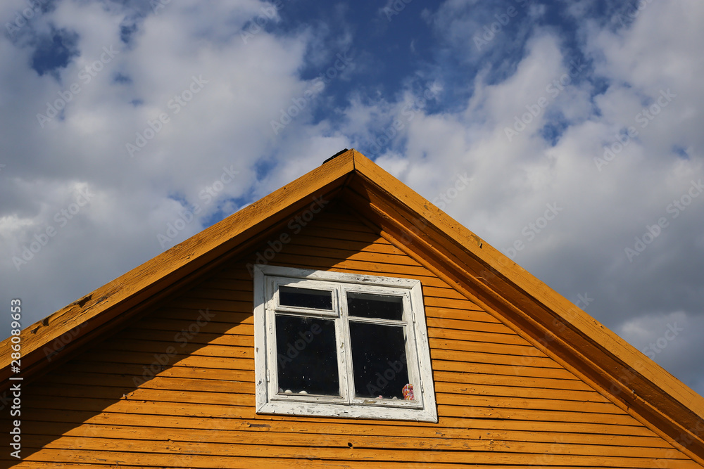 Part of typical house in Lithuania, Trakai. Antique old house. Triangular roof with yellow wooden walls and white windows and blue sky background.