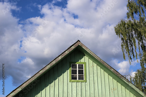 Triangular roof with green wooden walls and white windows and blue sky background. Part of typical house in Lithuania, Trakai. Antique old house