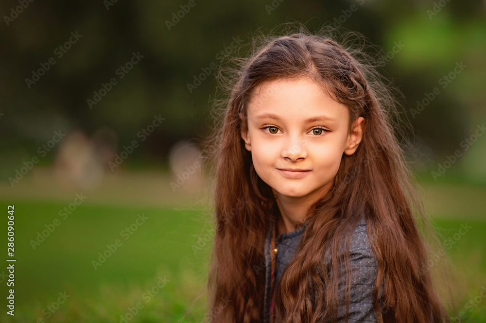 Fototapeta premium Happy smiling kid girl long hair on summer green grass background. Closeup