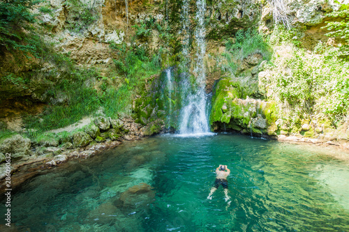 Man swimming in clear and cold water in natural pool under waterfall at forest