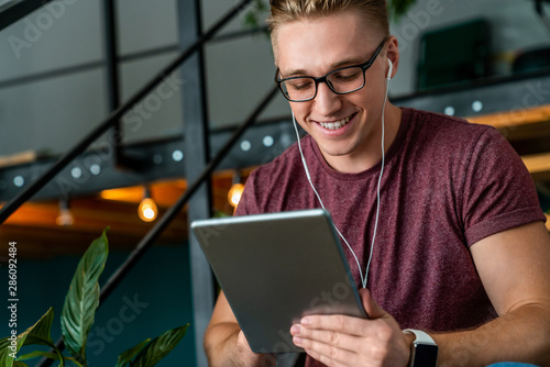 Young smiling man using digital tablet and headphones in the office