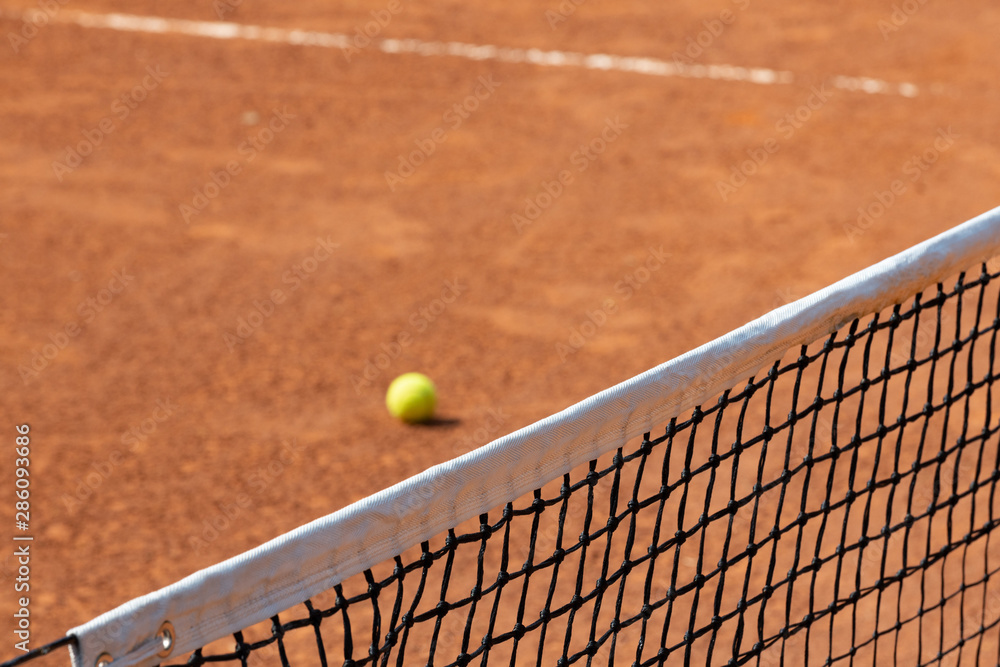 closeup of red clay tennis court net with yellow ball in the background