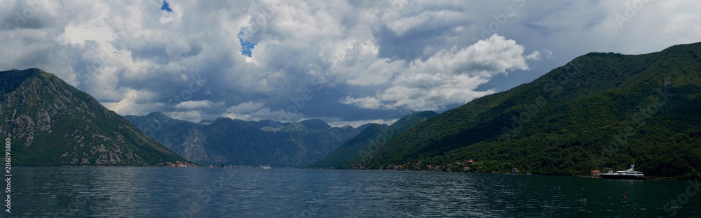 View of Boko Kotor on the background of mountains with clouds in the sky on a sunny day.