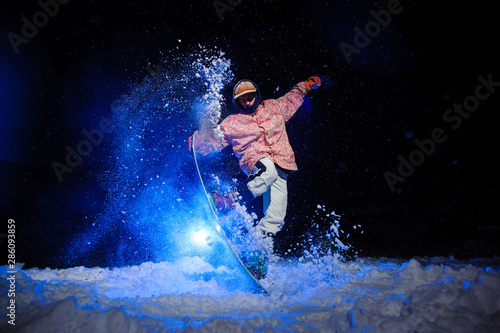 Active male snowboarder dressed in a white and pink sportswear performs tricks on the snow slope