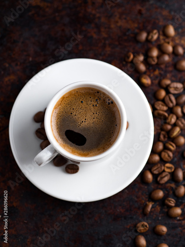 White espresso coffee Cup on vintage rusty background with scattered roasted coffee beans